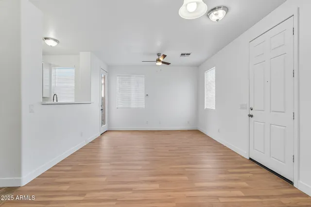 an empty room with wooden floor chandelier fan and windows