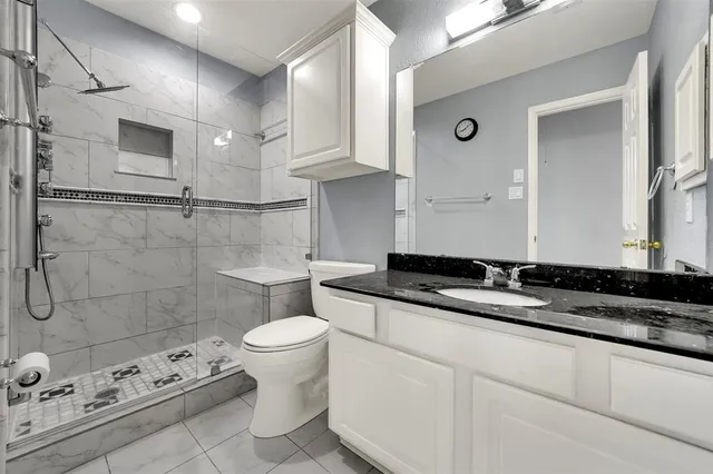 a bathroom with a granite countertop sink a toilet a mirror and shower