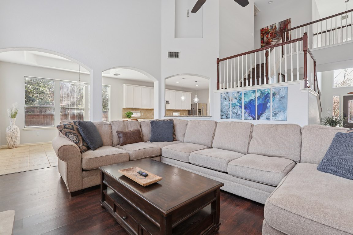 11217 Terrace Meadow Way Manor, TX 78653 - Photo 11 of 33 Living area featuring dark wood-type flooring, a towering ceiling, ceiling fan, stairs, and arched walkways