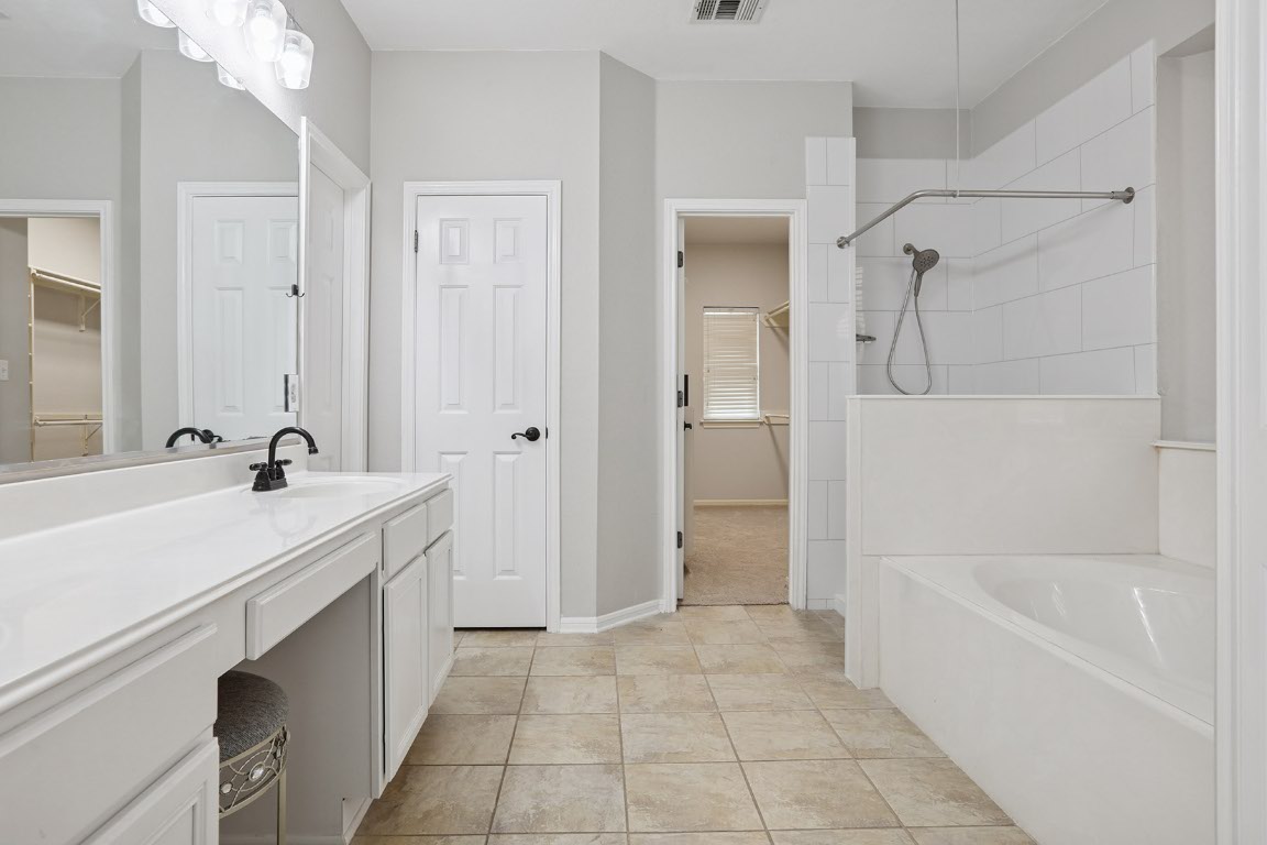 11217 Terrace Meadow Way Manor, TX 78653 - Photo 27 of 33 Bathroom with a spacious closet, vanity, a garden tub, and tiled shower