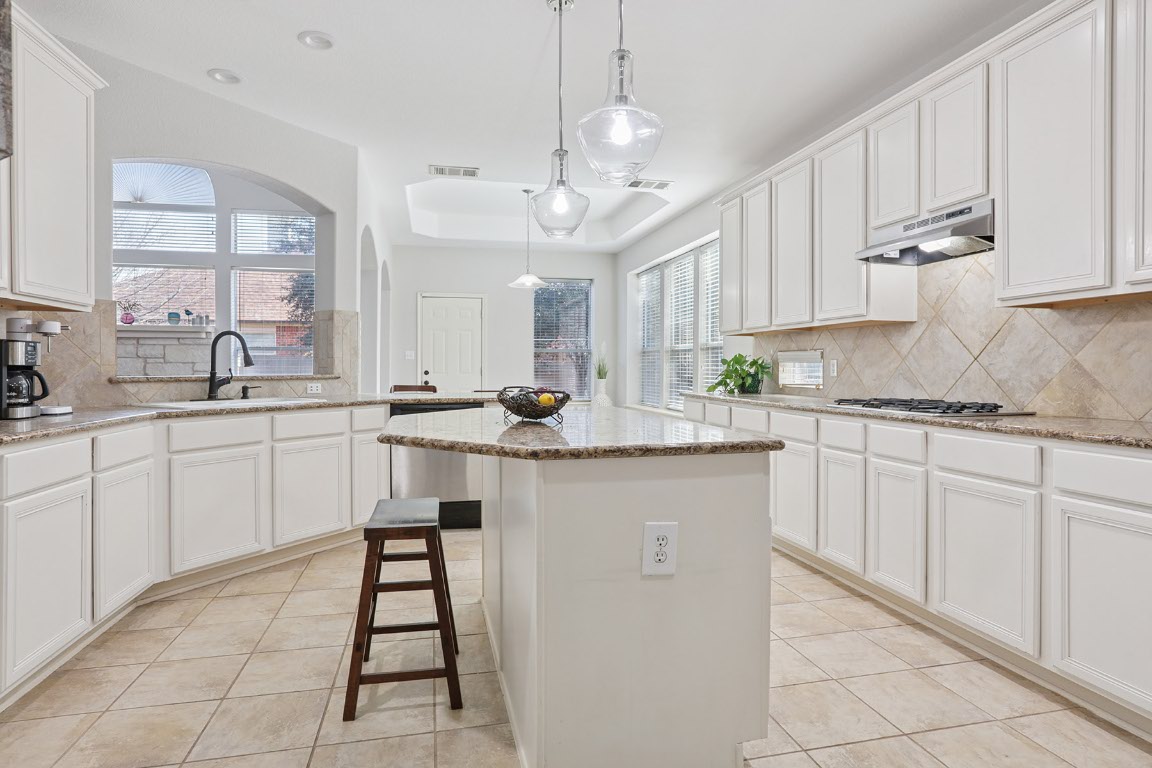 11217 Terrace Meadow Way Manor, TX 78653 - Photo 7 of 33 Kitchen featuring decorative backsplash, white cabinetry, light stone counters, and hanging light fixtures