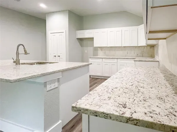 a large kitchen with kitchen island a stove a sink dishwasher a refrigerator and white cabinets with wooden floor