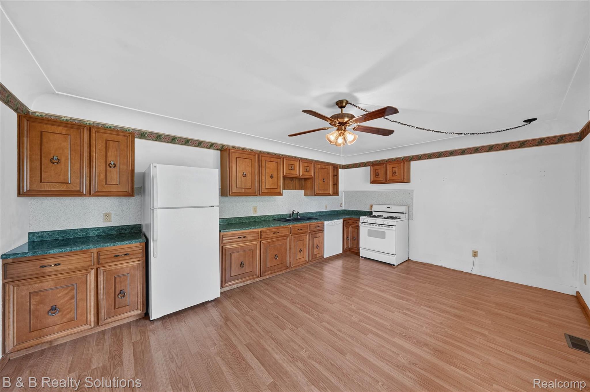 6605 Patrick Road North Branch, MI 48461 - Photo 7 of 44 Spacious kitchen featuring wood cabinetry with panel detailing, wood-finish flooring throughout, white refrigerator and range, teal-finish countertops, ceiling fan with integrated lighting, and ample counter and storage space