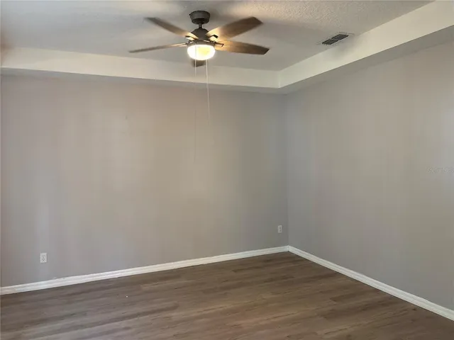 a view of an empty room with wooden floor and a ceiling fan