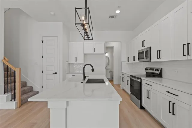 a kitchen with stainless steel appliances a sink dishwasher stove refrigerator and white cabinets with wooden floor