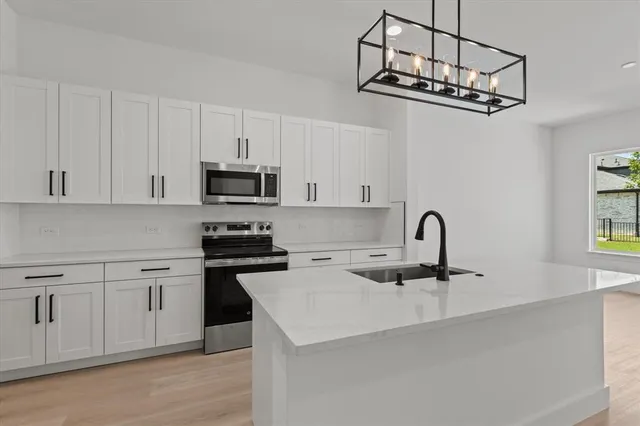 a kitchen with stainless steel appliances a sink dishwasher a stove top oven a refrigerator with white cabinets and wooden floor