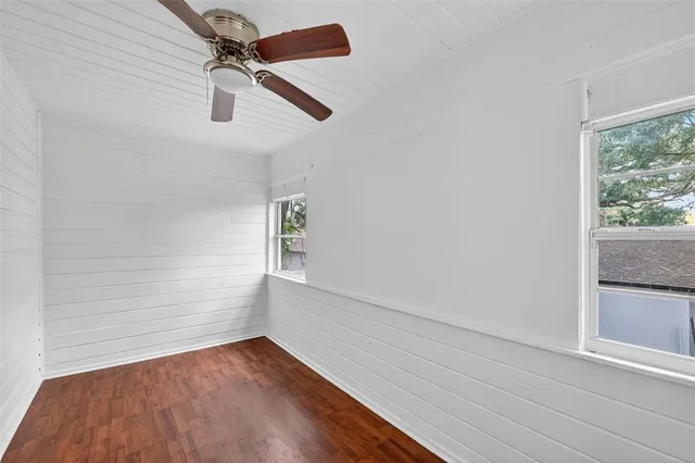 an empty room with wooden floor fan and windows