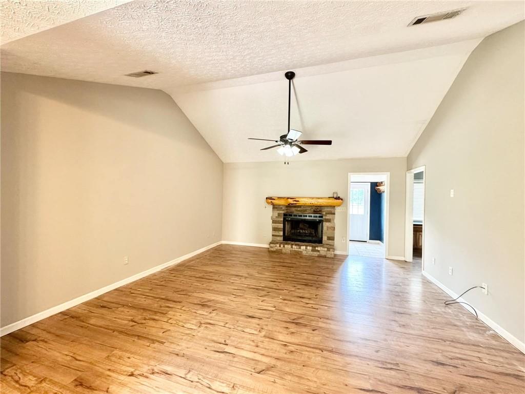 280 Owens Road Fort Mitchell, AL 36856 - Photo 7 of 56 Unfurnished living room featuring ceiling fan, lofted ceiling, light wood finished floors, a fireplace with raised hearth, and baseboards
