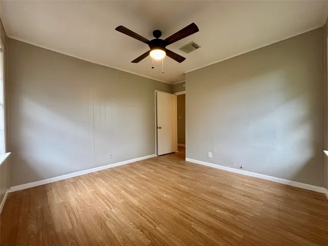 a view of an empty room with wooden floor and a ceiling fan