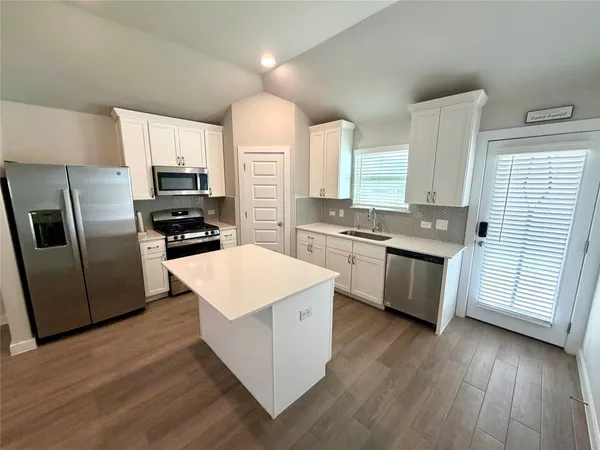 a kitchen with stainless steel appliances a microwave a stove a sink a refrigerator white cabinets and wooden floor