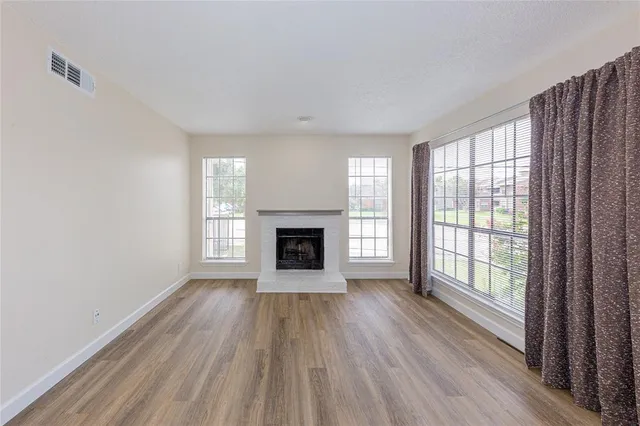a view of an empty room with wooden floor fire place and windows
