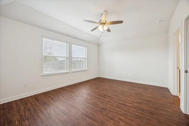 an empty room with wooden floor fan and windows