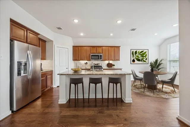 a kitchen with stainless steel appliances granite countertop a refrigerator a stove a sink a dining table and chairs with wooden floor