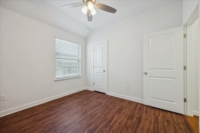an empty room with wooden floor chandelier fan and windows