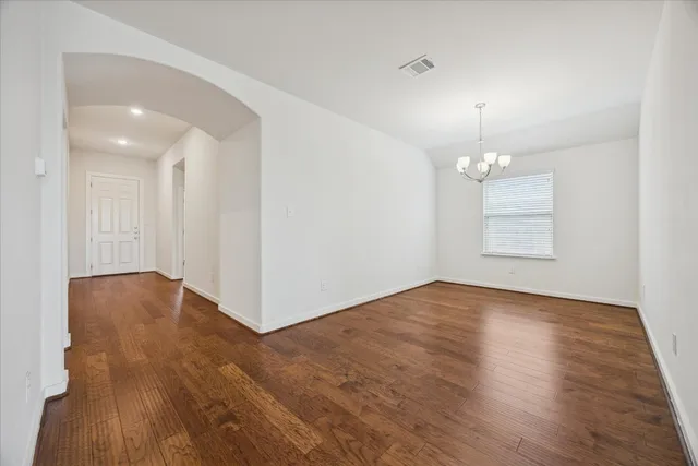 a view of empty room with wooden floor and kitchen