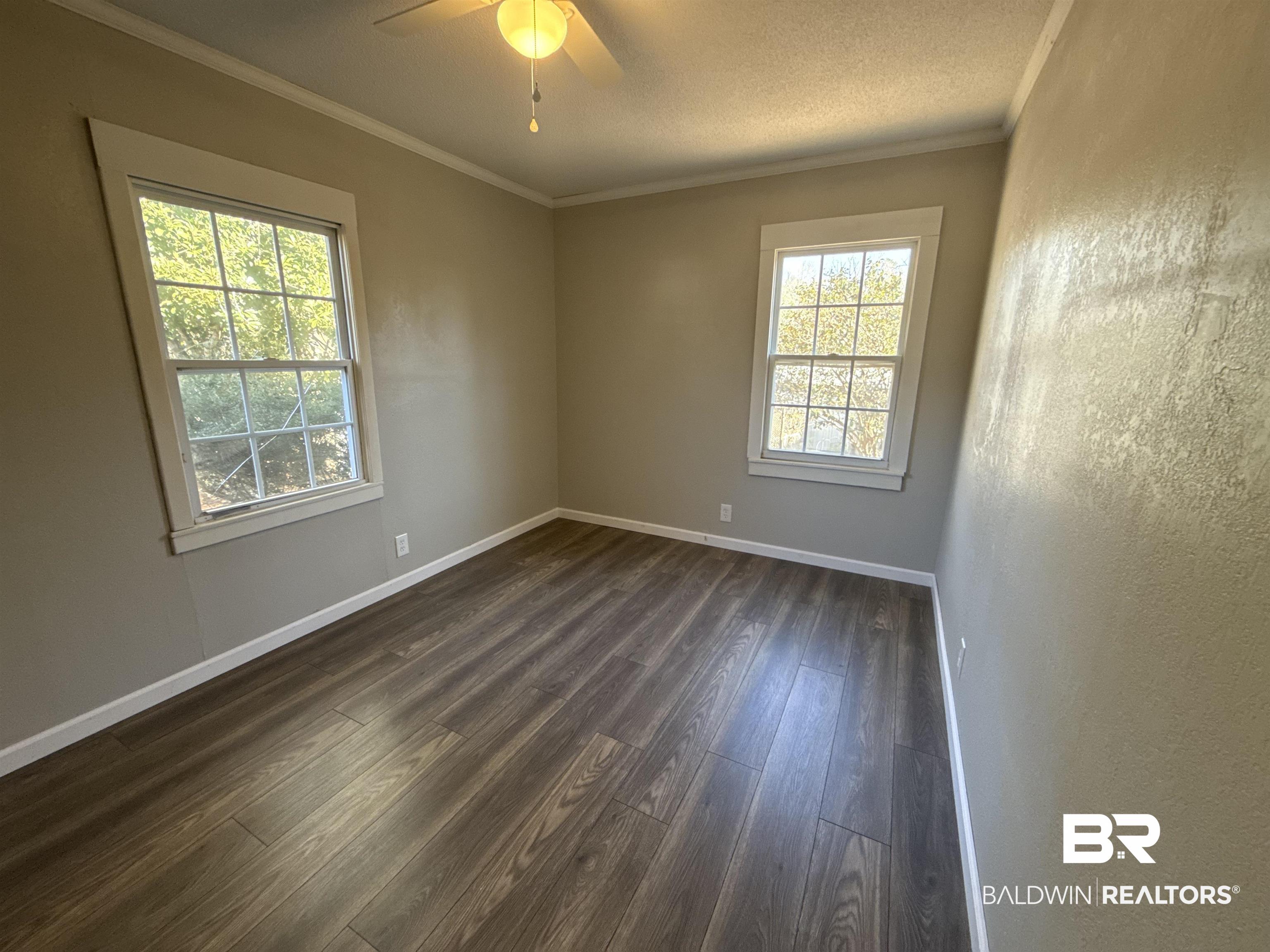 32 Slate Street Atmore, AL 36502 - Photo 11 of 16 Empty room featuring dark wood finished floors, ceiling fan, ornamental molding, a textured ceiling, and a textured wall