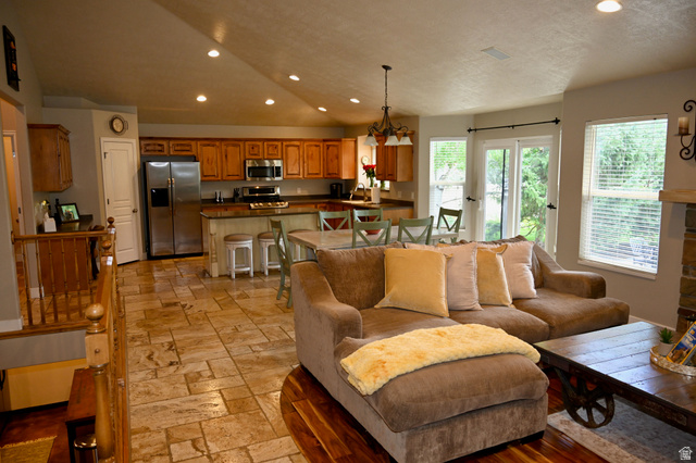 314 Brown Farm Lane Draper, UT 84020 - Photo 8 of 57 Expansive living area featuring vaulted ceilings with recessed lighting, large windows, a stone-clad fireplace, and a kitchen with wood cabinetry and stainless steel appliances