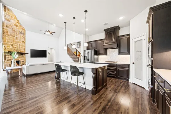 a kitchen with stainless steel appliances kitchen island granite countertop a refrigerator a stove top oven a sink dishwasher a dining table and chairs with wooden floor