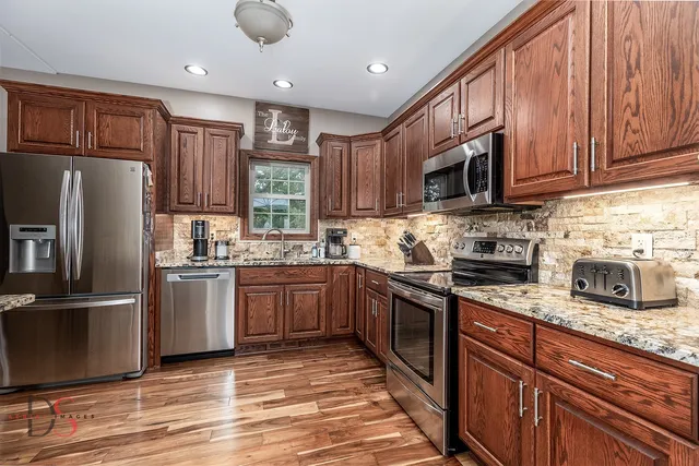 a kitchen with stainless steel appliances granite countertop a stove top oven a sink dishwasher a dining table and chairs with wooden floor