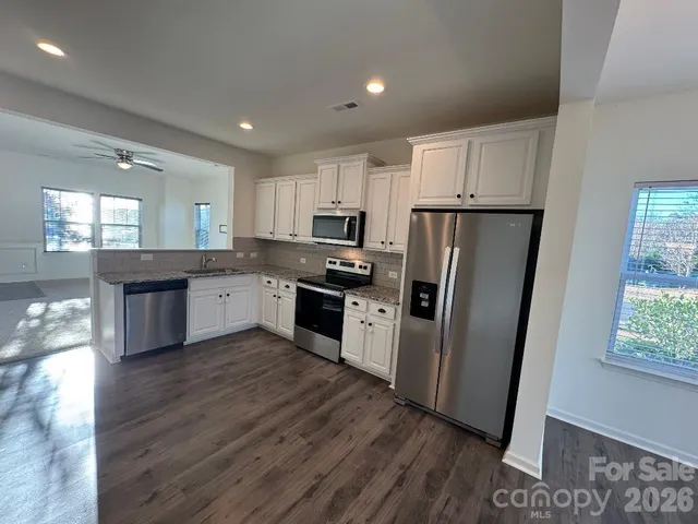 a kitchen with granite countertop a refrigerator a sink dishwasher a stove and white cabinets with wooden floor