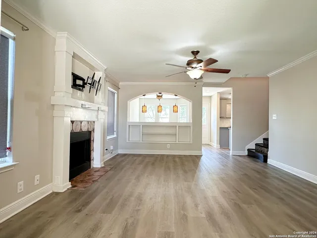 wooden floor in an empty room with a fireplace and a kitchen