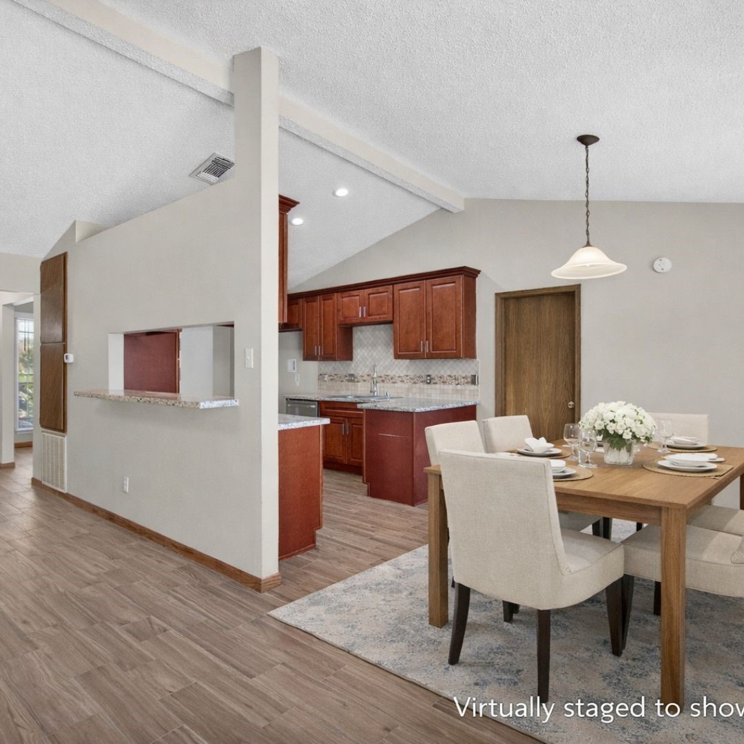 11803 Inga Lane Houston, TX 77064 - Photo 13 of 39 This photo showcases a bright, open-concept dining and kitchen area with wooden flooring. The kitchen features cherry wood cabinets, granite countertops, and a pass-through window. The dining space is elegantly staged with a wooden table and upholstered chairs, under a modern pendant light.