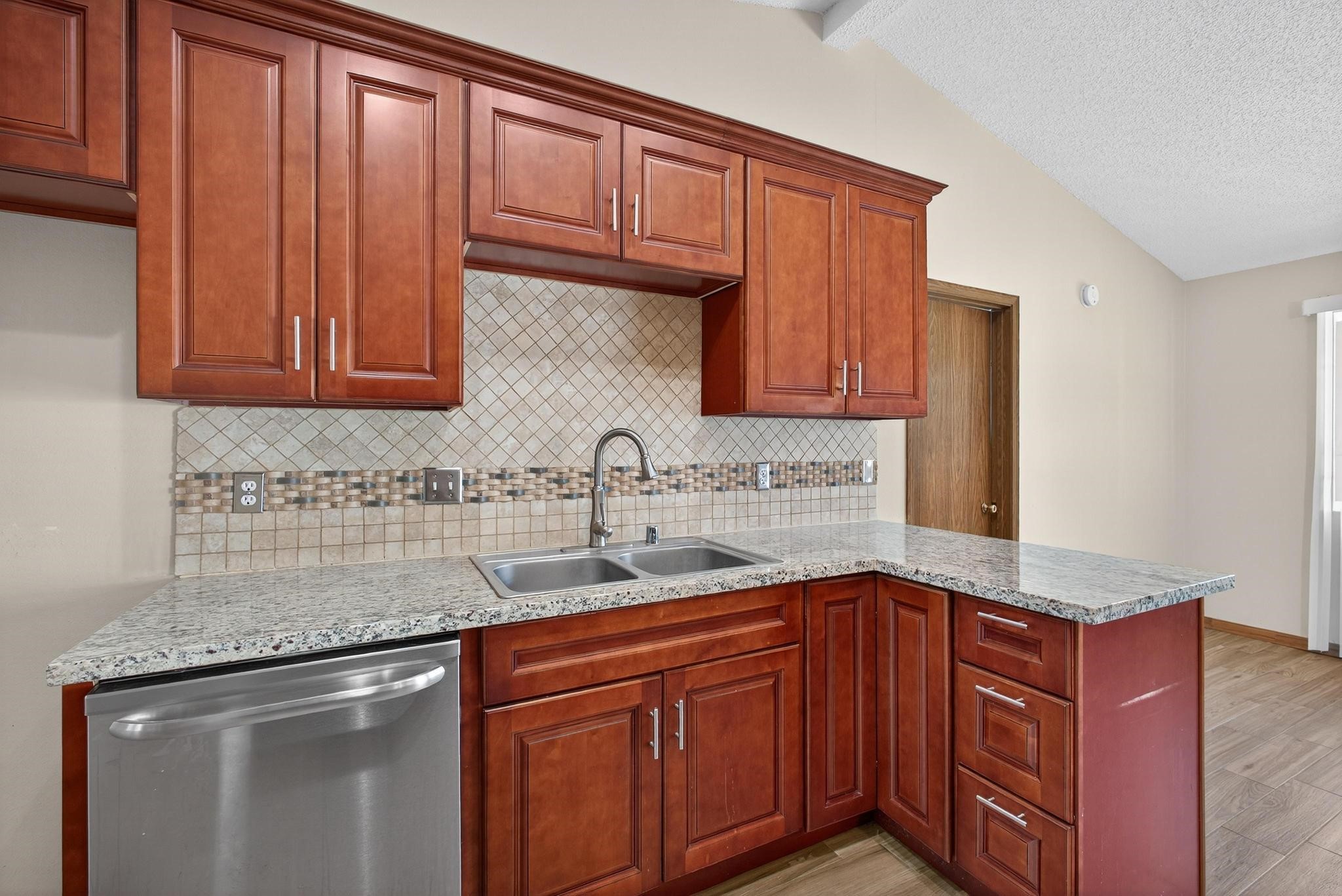 11803 Inga Lane Houston, TX 77064 - Photo 16 of 39 This kitchen features elegant wooden cabinets, a granite countertop, stainless steel dishwasher, and a stylish tiled backsplash. The open layout offers ample storage and workspace, perfect for cooking and entertaining.