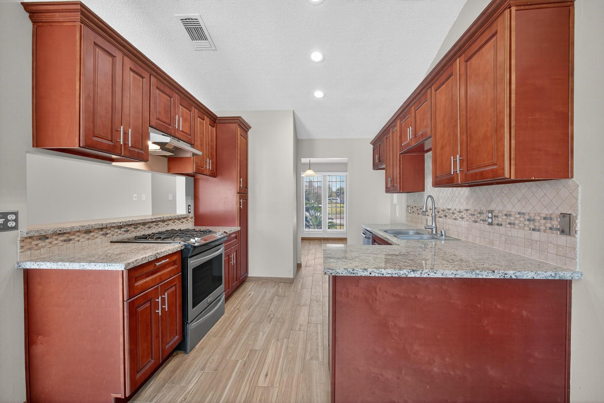 11803 Inga Lane Houston, TX 77064 - Photo 18 of 39 This kitchen features rich wooden cabinetry, granite countertops, and stainless steel appliances. It has a modern tile backsplash, a gas stove, and ample natural light from a large window.