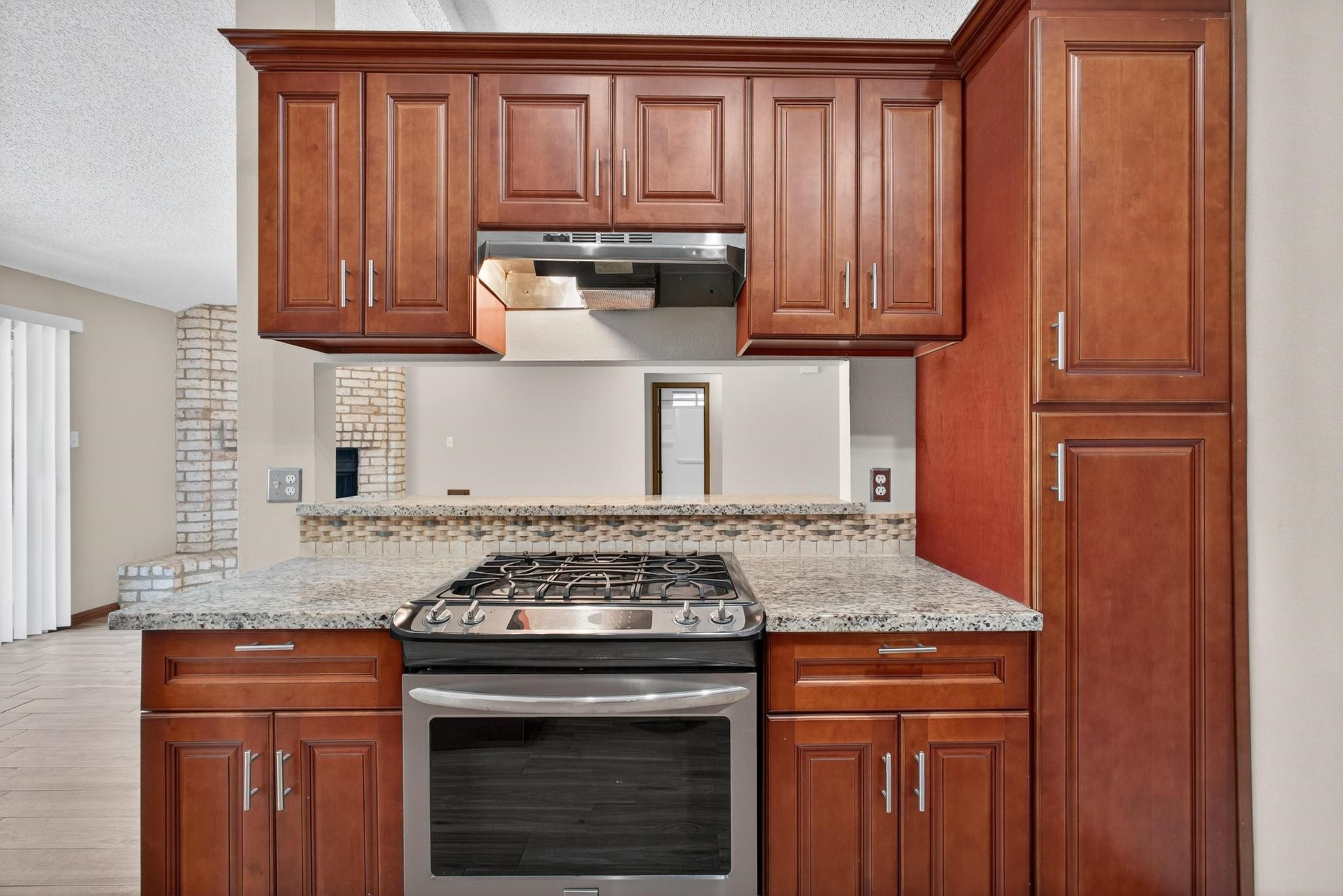 11803 Inga Lane Houston, TX 77064 - Photo 19 of 39 This kitchen features elegant wooden cabinetry, a modern stainless steel gas stove, and granite countertops. The open layout includes a passthrough window, enhancing connectivity with adjacent living spaces.
