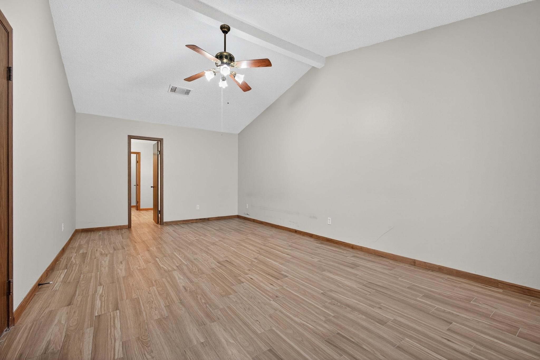 11803 Inga Lane Houston, TX 77064 - Photo 21 of 39 This spacious room features a vaulted ceiling with a ceiling fan, light gray walls, and wood-like flooring, creating a warm and inviting atmosphere. A doorway leads to an adjoining room, enhancing the open feel.