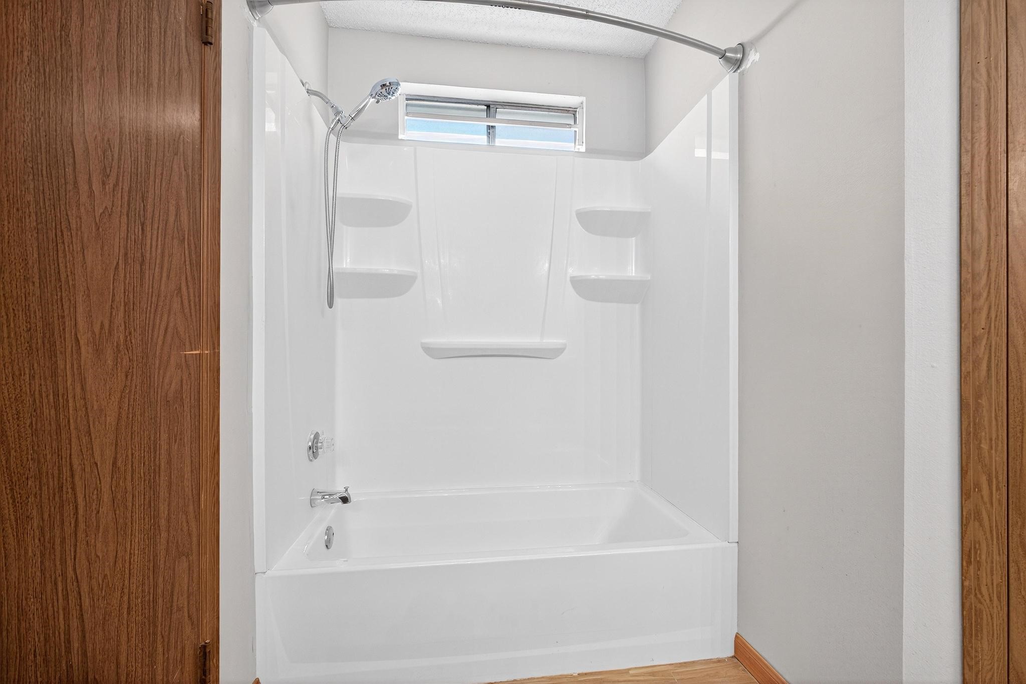11803 Inga Lane Houston, TX 77064 - Photo 27 of 39 This bathroom features a clean, white bathtub and shower combo with built-in shelving. It has a small window for natural light and is framed by warm wood accents.