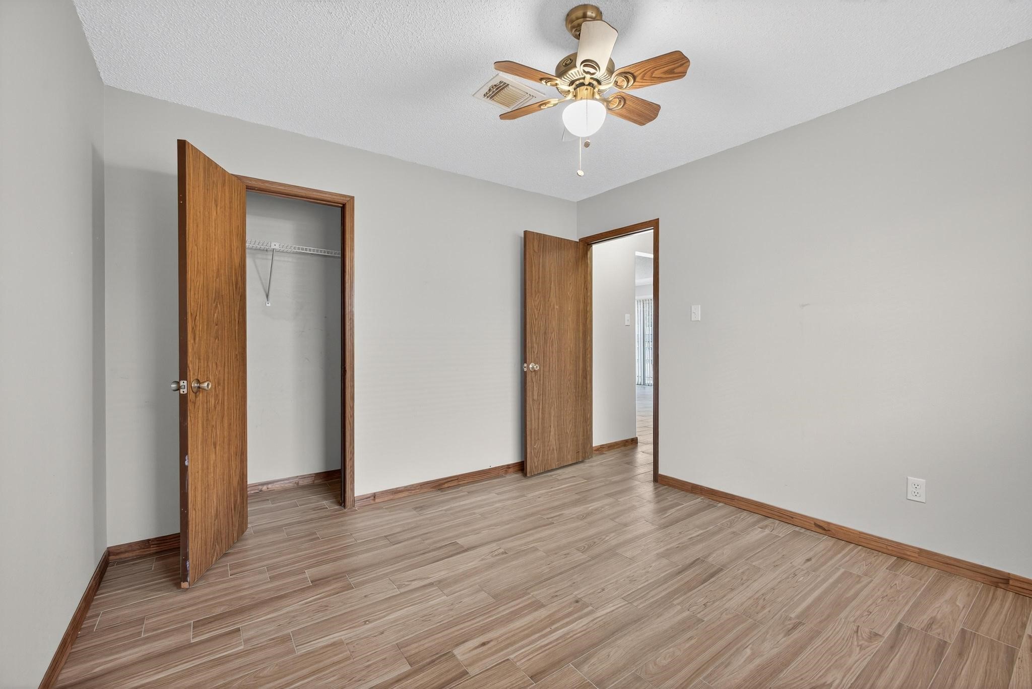 11803 Inga Lane Houston, TX 77064 - Photo 32 of 39 This is a bright, empty bedroom with wood-style flooring, neutral walls, a ceiling fan, and a small closet. It features wooden doors and trim, creating a warm, inviting space.
