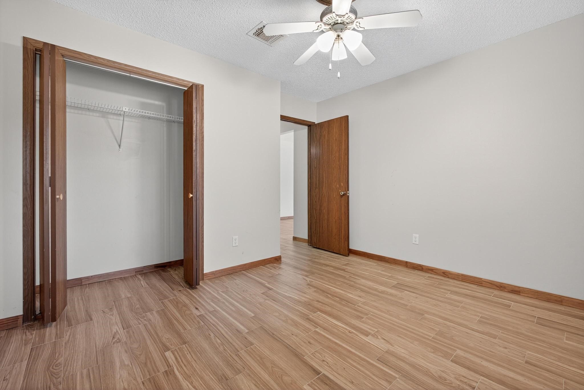11803 Inga Lane Houston, TX 77064 - Photo 33 of 39 This photo shows a bright, empty room with wood flooring and neutral walls. It features a ceiling fan, an open closet with sliding doors, and a doorway leading to another space.