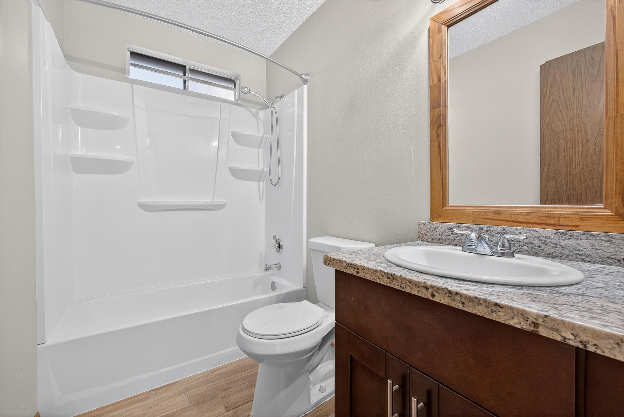11803 Inga Lane Houston, TX 77064 - Photo 37 of 39 This bathroom features a clean, modern design with a white tub-shower combo, a granite countertop, and a wood-framed mirror above the sink. The neutral tones and simple layout offer a bright and functional space.