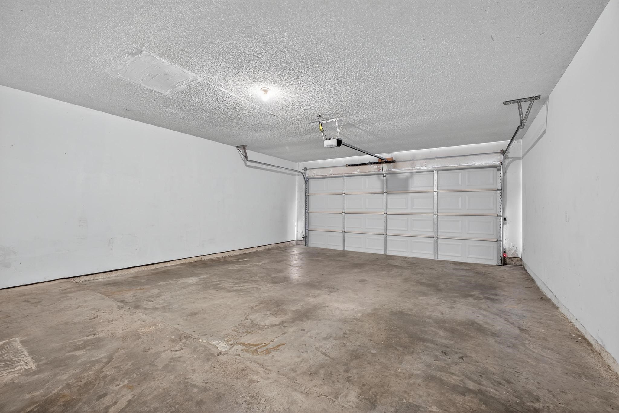 11803 Inga Lane Houston, TX 77064 - Photo 38 of 39 This photo shows a spacious, empty garage with a concrete floor and a large, automatic door. The walls and ceiling are plain, offering a clean slate for customization. Ideal for parking or storage.