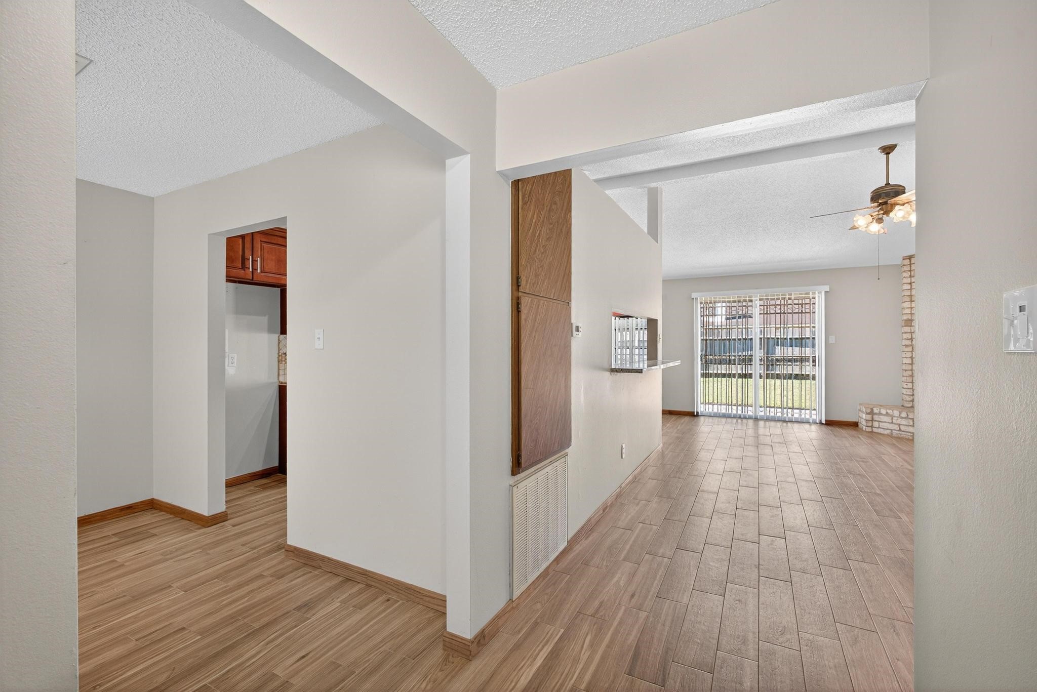 11803 Inga Lane Houston, TX 77064 - Photo 7 of 39 Bright open-concept living area with wood-style flooring and large windows leading to a patio. Features a ceiling fan and an adjoining kitchen area with warm wooden cabinets.