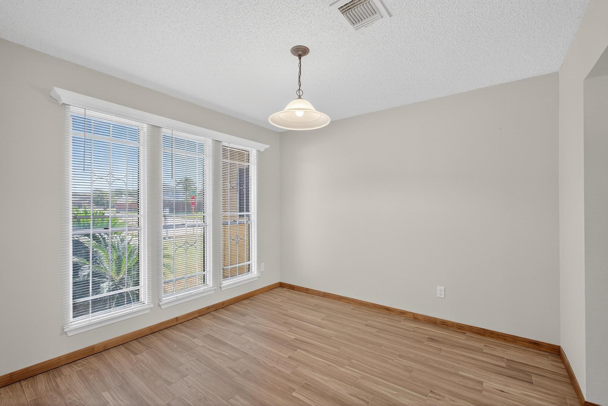 11803 Inga Lane Houston, TX 77064 - Photo 9 of 39 This photo shows a bright dining room with light wood flooring, neutral walls, and large windows with blinds, allowing plenty of natural light. A ceiling light fixture adds a cozy touch.