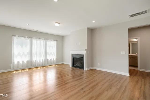 an empty room with wooden floor fireplace and windows