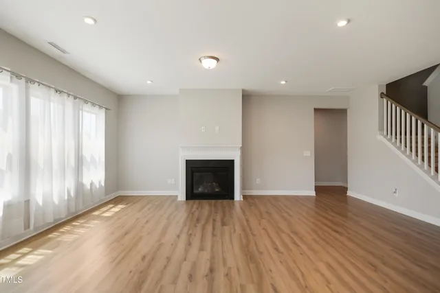 an empty room with wooden floor a fireplace and windows