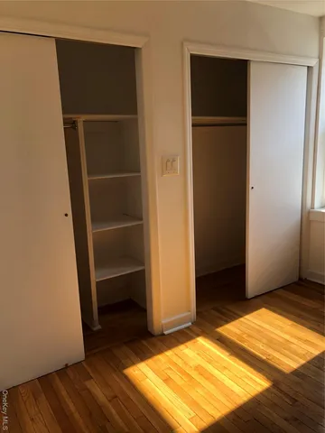 a view of an empty room with wooden floor and closet