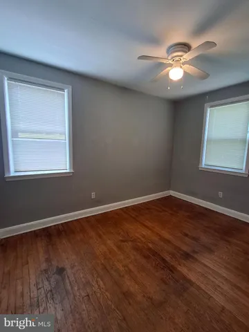 an empty room with wooden floor chandelier fan and windows