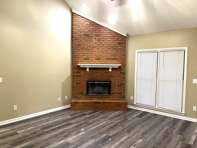 a view of an empty room with wooden floor fireplace and a window