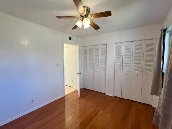 an empty room with wooden floor fan and windows