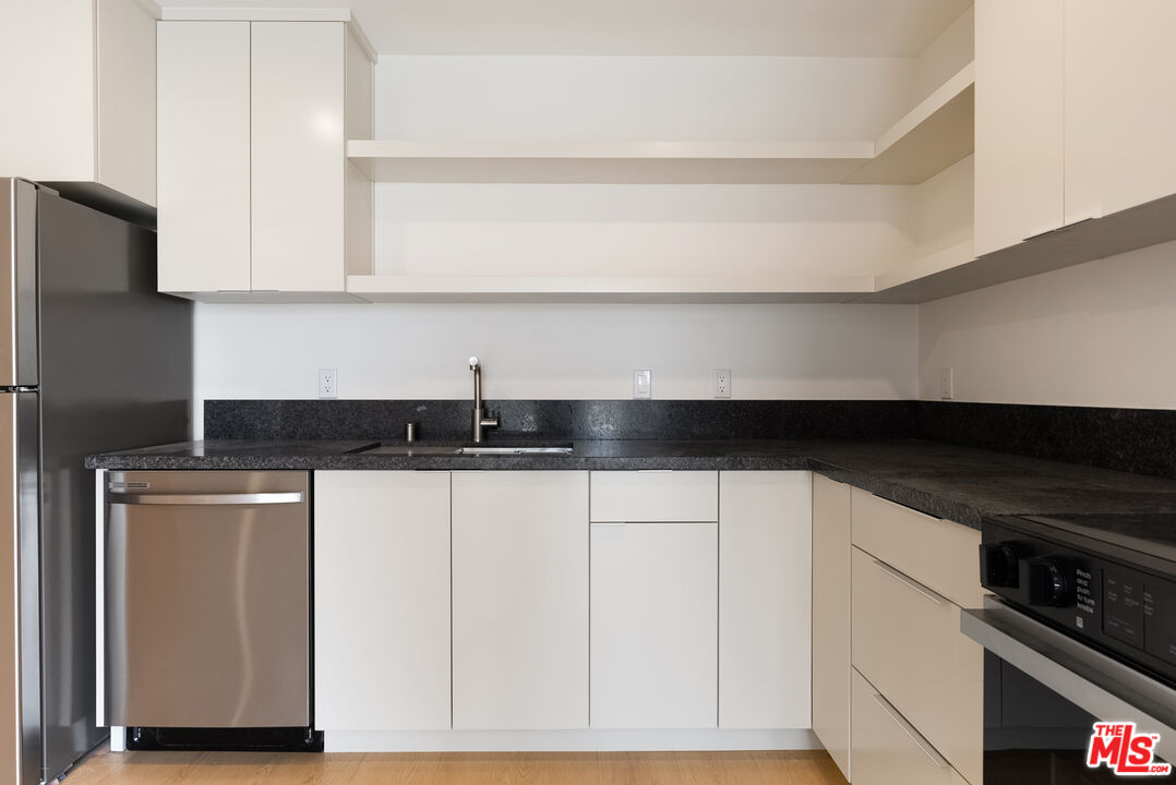 8561 Belmont Street, Unit 4 Cypress, CA 90630 - Photo 6 of 23 a kitchen with granite countertop white cabinets and black appliances
