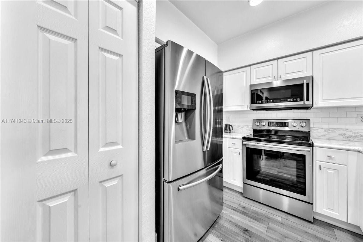 8381 Southwest 26 Th Street, Unit 103 Miramar, FL 33025 - Photo 16 of 62 a kitchen with stainless steel appliances granite countertop a refrigerator a microwave oven with white cabinets and wooden floor