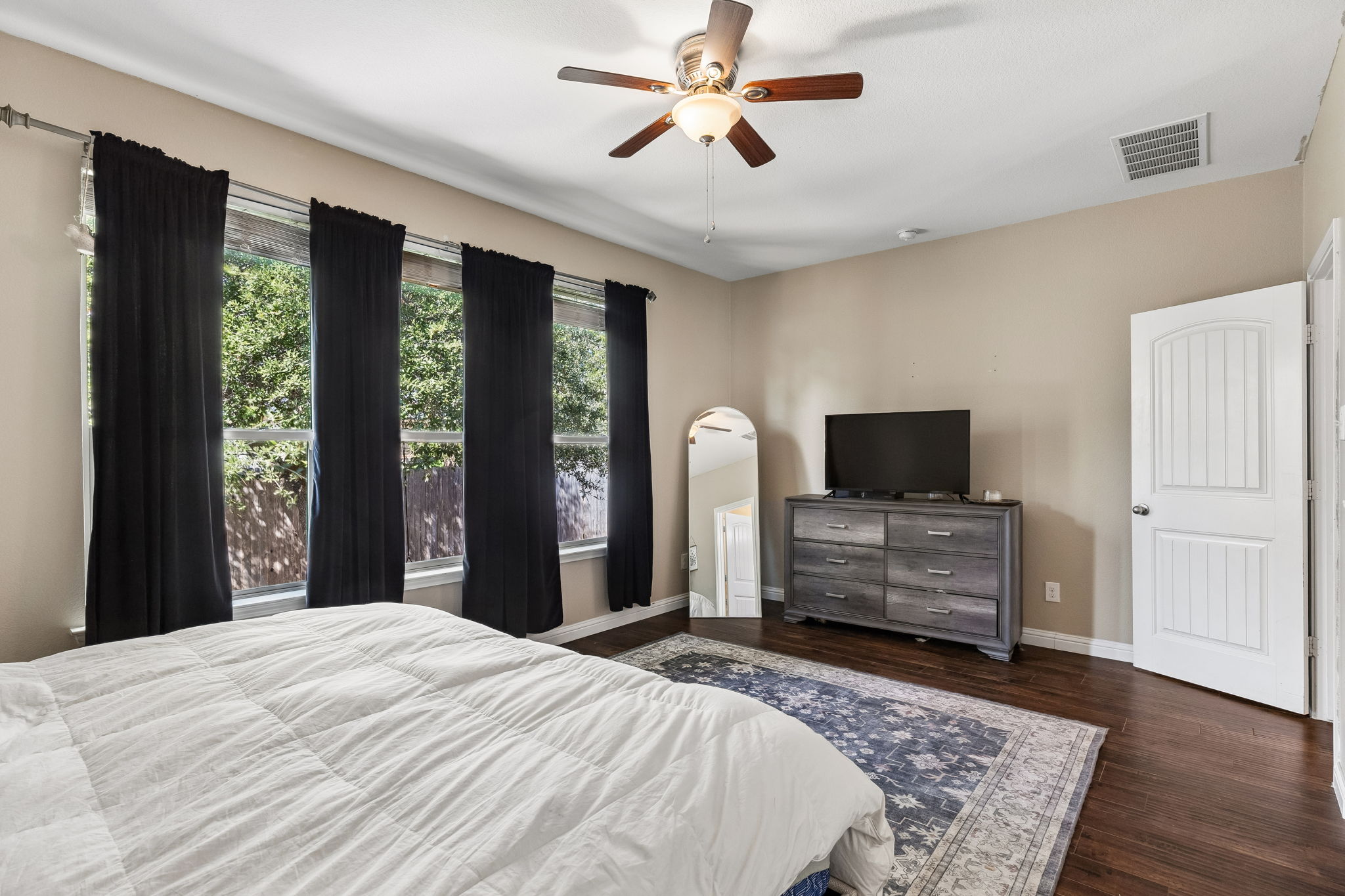 1113 Yellow Iris Road Leander, TX 78641 - Photo 13 of 26 Rich wood flooring anchors this bedroom featuring tall windows looking out to backyard greenery.