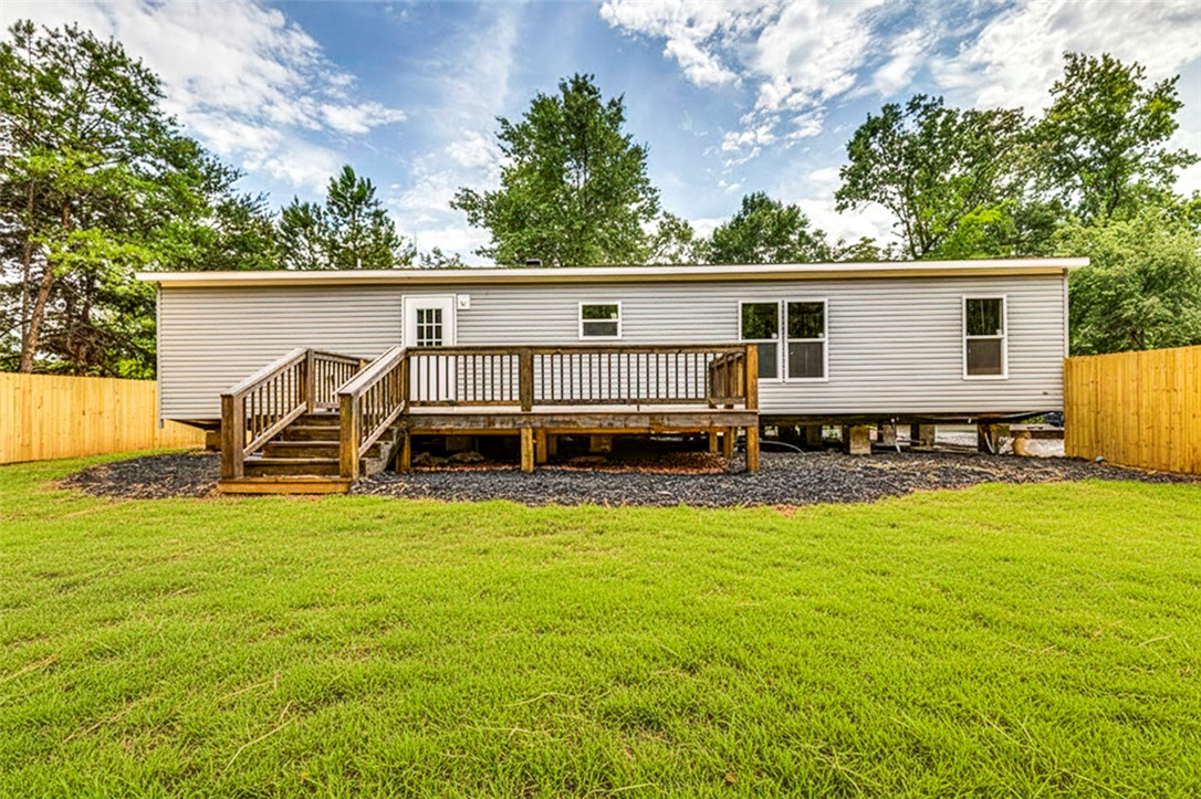 474 Bryant Road Pelzer, SC 29669 - Photo 7 of 42 A classic manufactured home features a broad deck overlooking a verdant lawn, secured by a privacy fence.