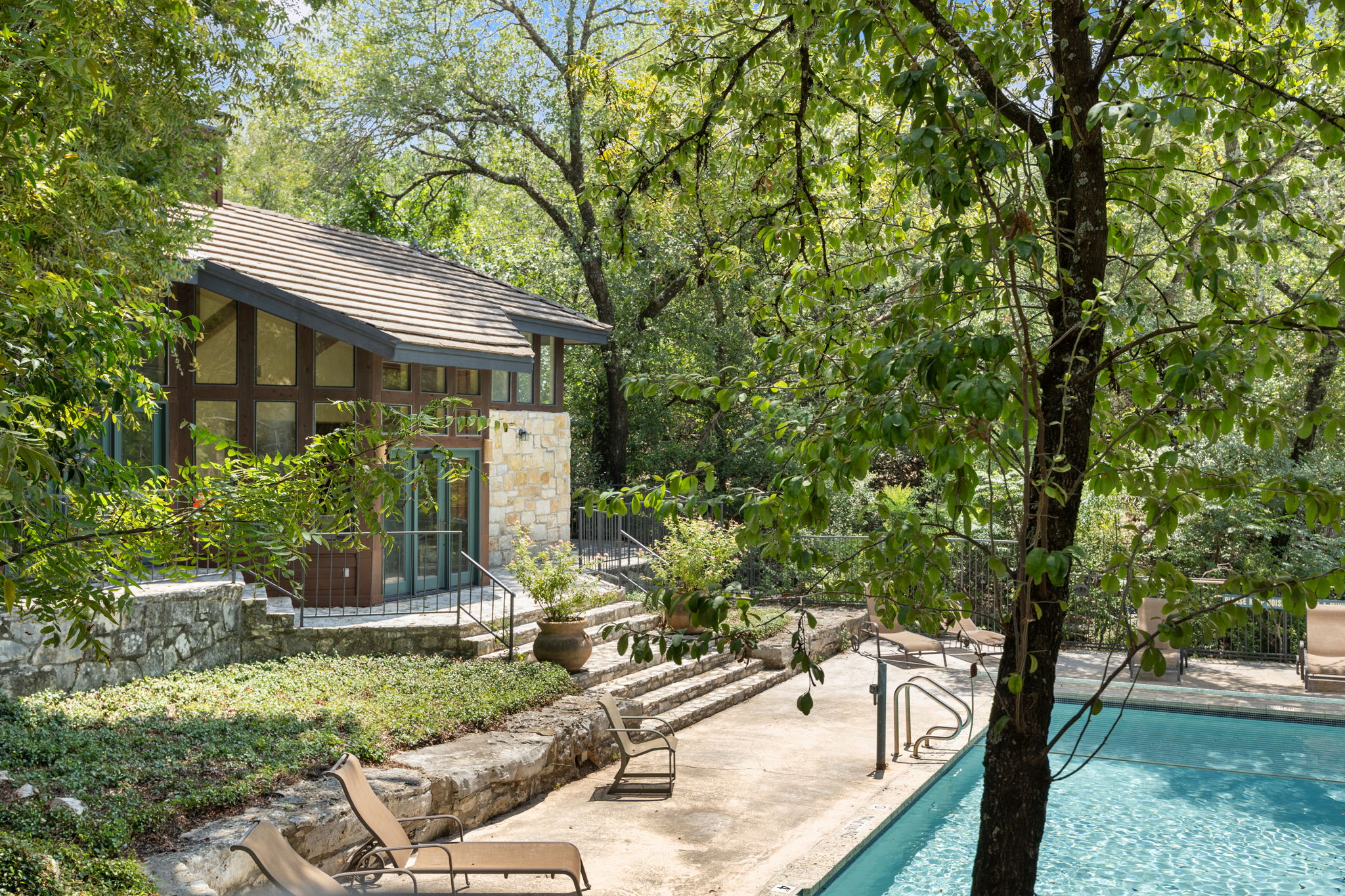 4711 Spicewood Springs Road, Unit 1106 Austin, TX 78759 - Photo 17 of 19 Exterior featuring a stone and wood facade with large windows, an angled roofline, and a private swimming pool with stone coping