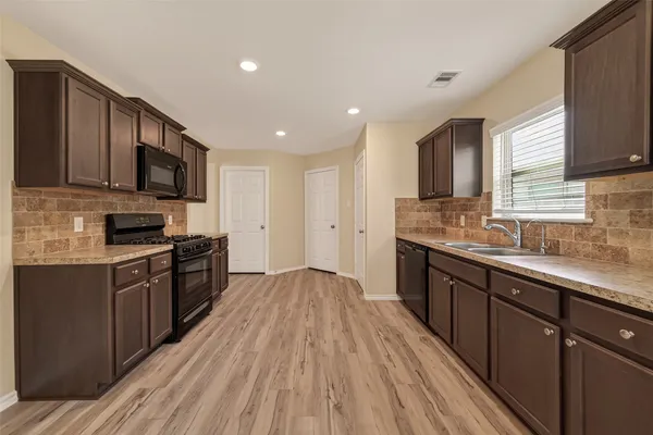 a kitchen with stainless steel appliances granite countertop wooden cabinets a stove top oven a sink and dishwasher with wooden floor