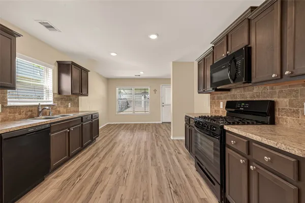 a kitchen with stainless steel appliances granite countertop a stove top oven a sink dishwasher a refrigerator and a microwave oven with wooden floor